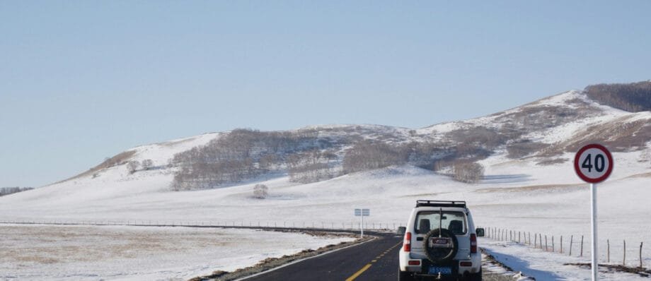 A car driving on a road in Mongolia's countryside and the landscape is covered in snow.