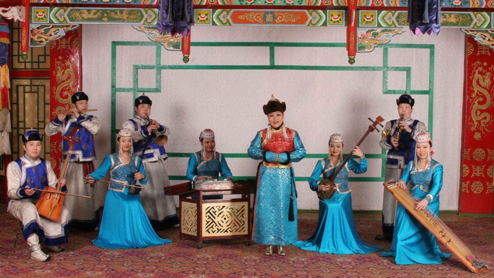 Image of the Tumen Ekh Folk group performing. There are 9 members playing tradicional Mongolian instruments and singing